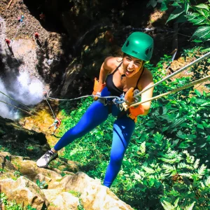 Smiling woman rappelling down a waterfall in the tropical jungle of Costa Rica