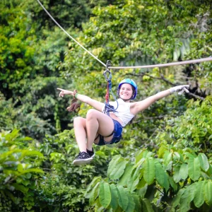 Smiling woman ziplining above the lush rainforest in La Fortuna with Wave Canopy Tour